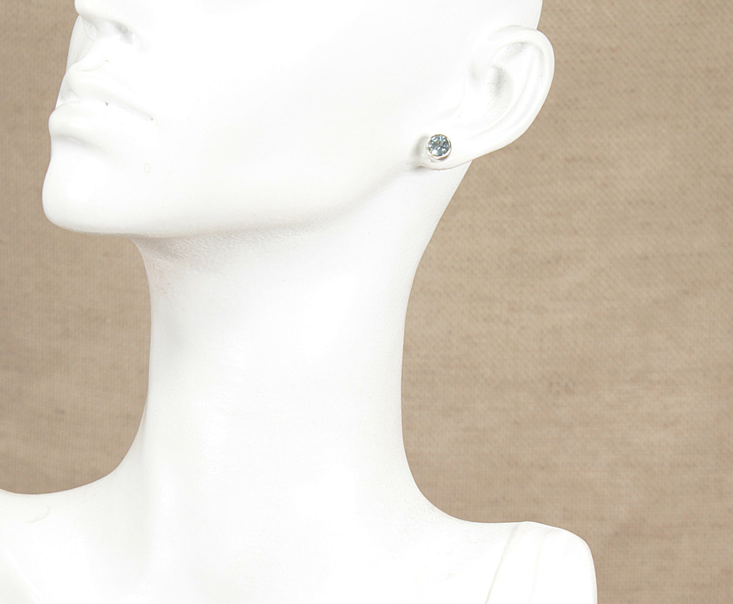 Silver blue topaz stud earring on a white mannequin ear against a beige background