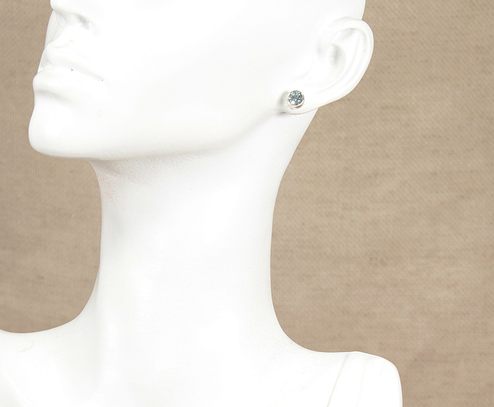 Silver blue topaz stud earring on a white mannequin ear against a beige background