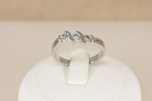 Silver ring with three blue topaz gemstones on a white stand against a beige background