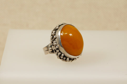 A butterscotch amber stone set in a silver ring with floral inspired detailing on the sides, displayed against a neutral background.
