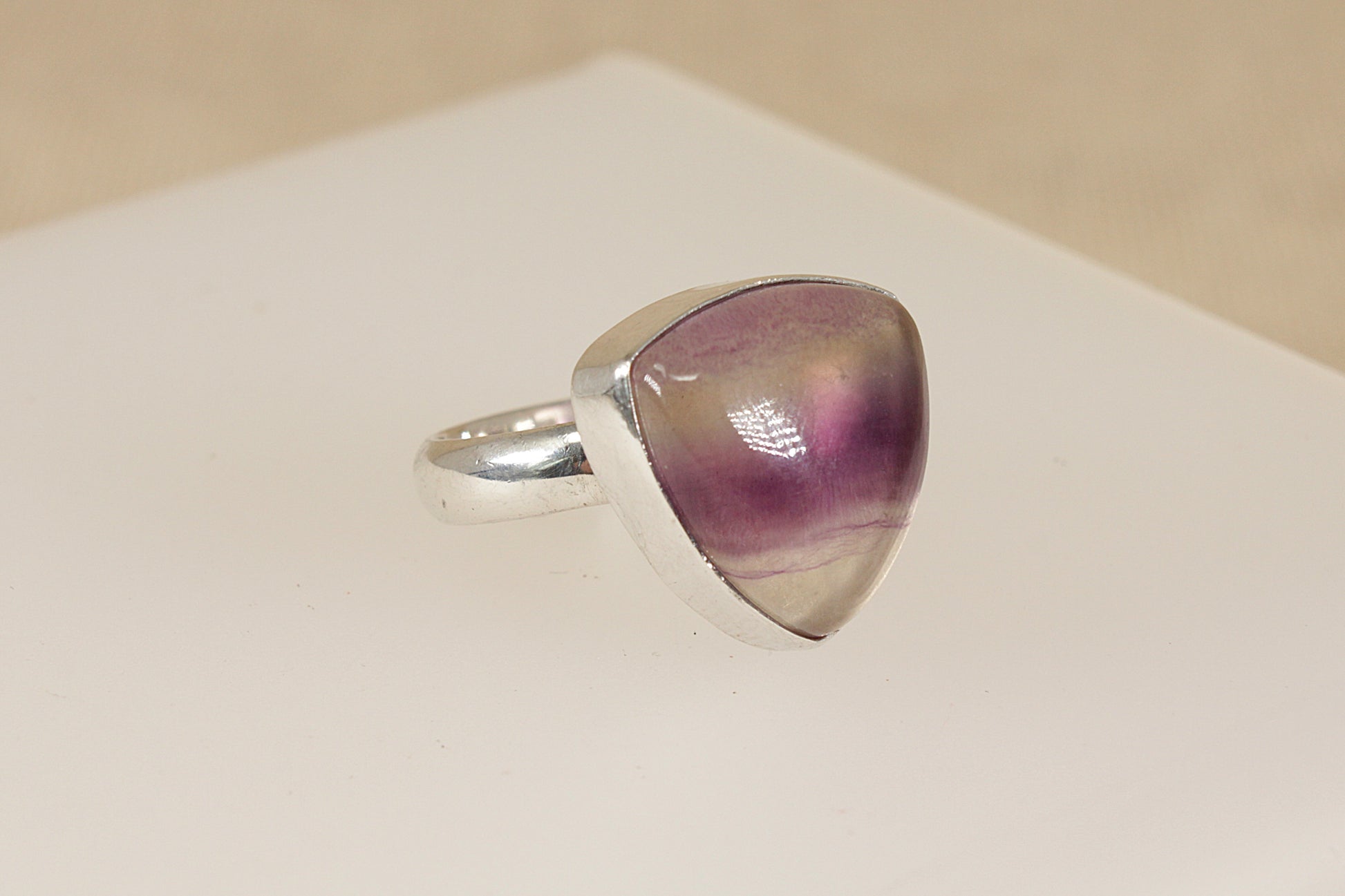 Silver ring with a triangular purple banded fluorite gemstone on a beige background