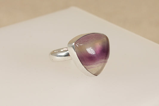 Silver ring with a triangular purple banded fluorite gemstone on a beige background