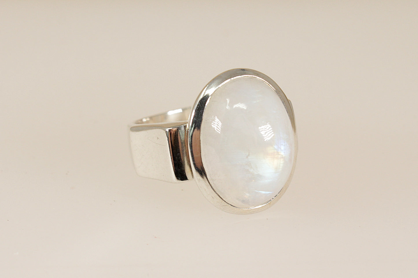 Silver ring with a large, round, cabochon moonstone gemstone on a beige background