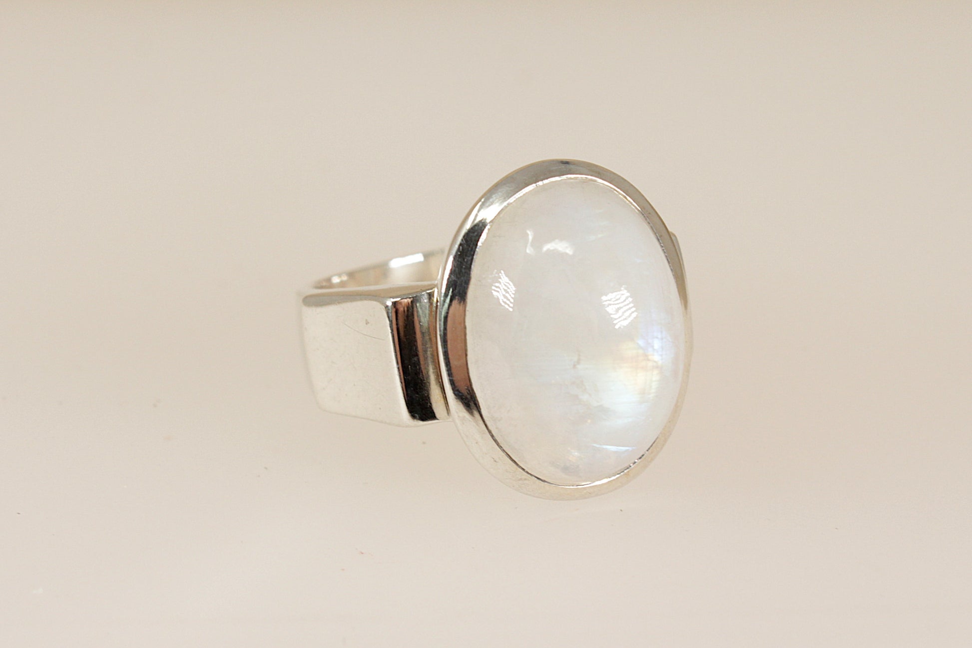 Silver ring with a large, round, cabochon moonstone gemstone on a beige background