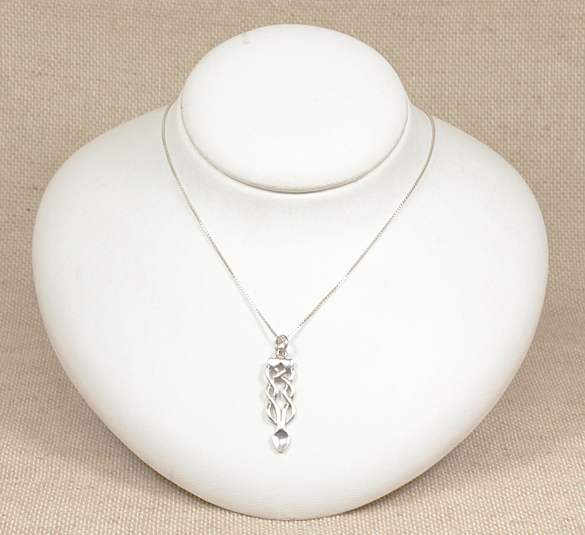 A silver Celtic knot pendant necklace displayed on a white mannequin bust against a beige background.