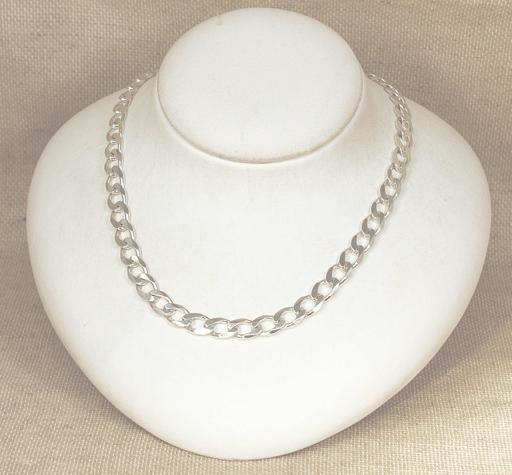 Silver flat curb link necklace chain on a white bust against a beige background