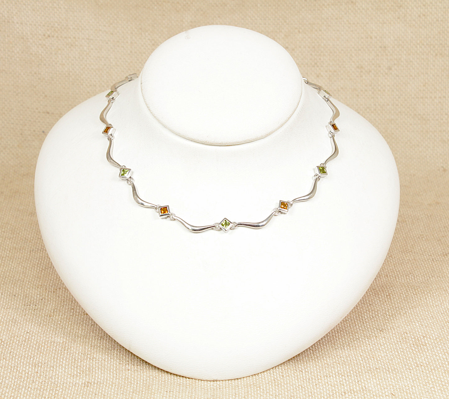 A sterling silver necklace with alternating square bezel-set citrine and peridot gemstones, displayed on a white mannequin.