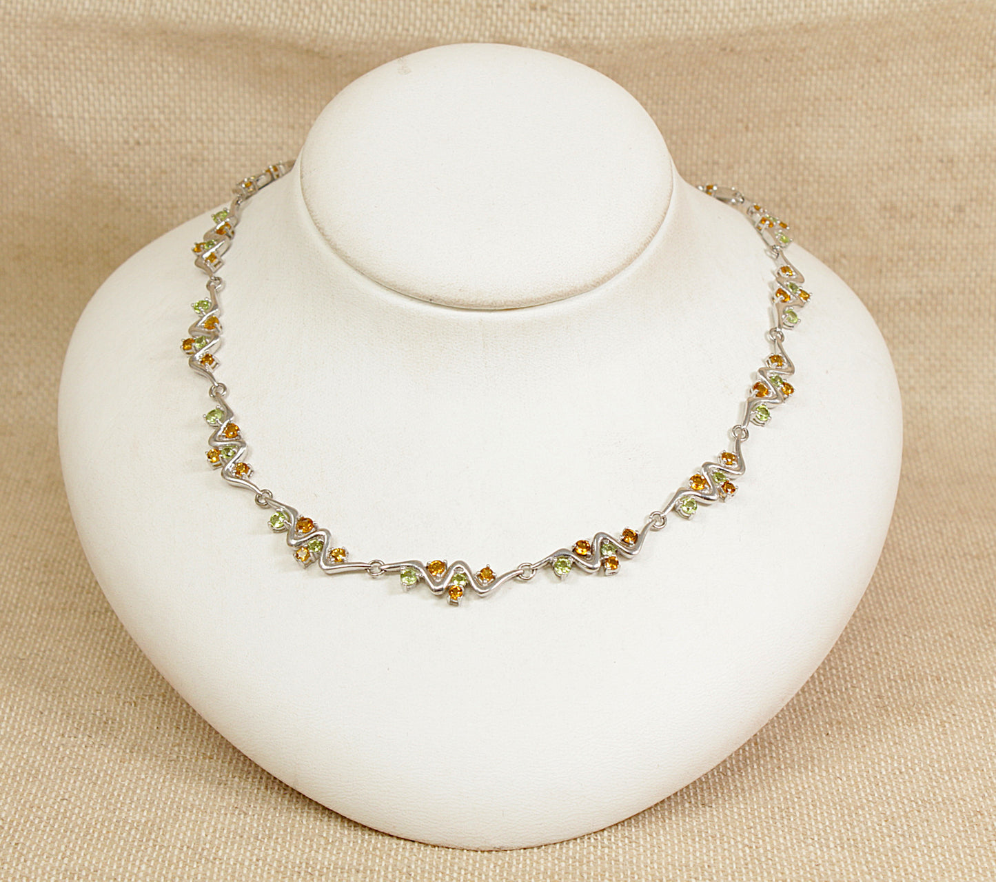 Necklace with citrine and peridot gemstones on a white stand against a beige background