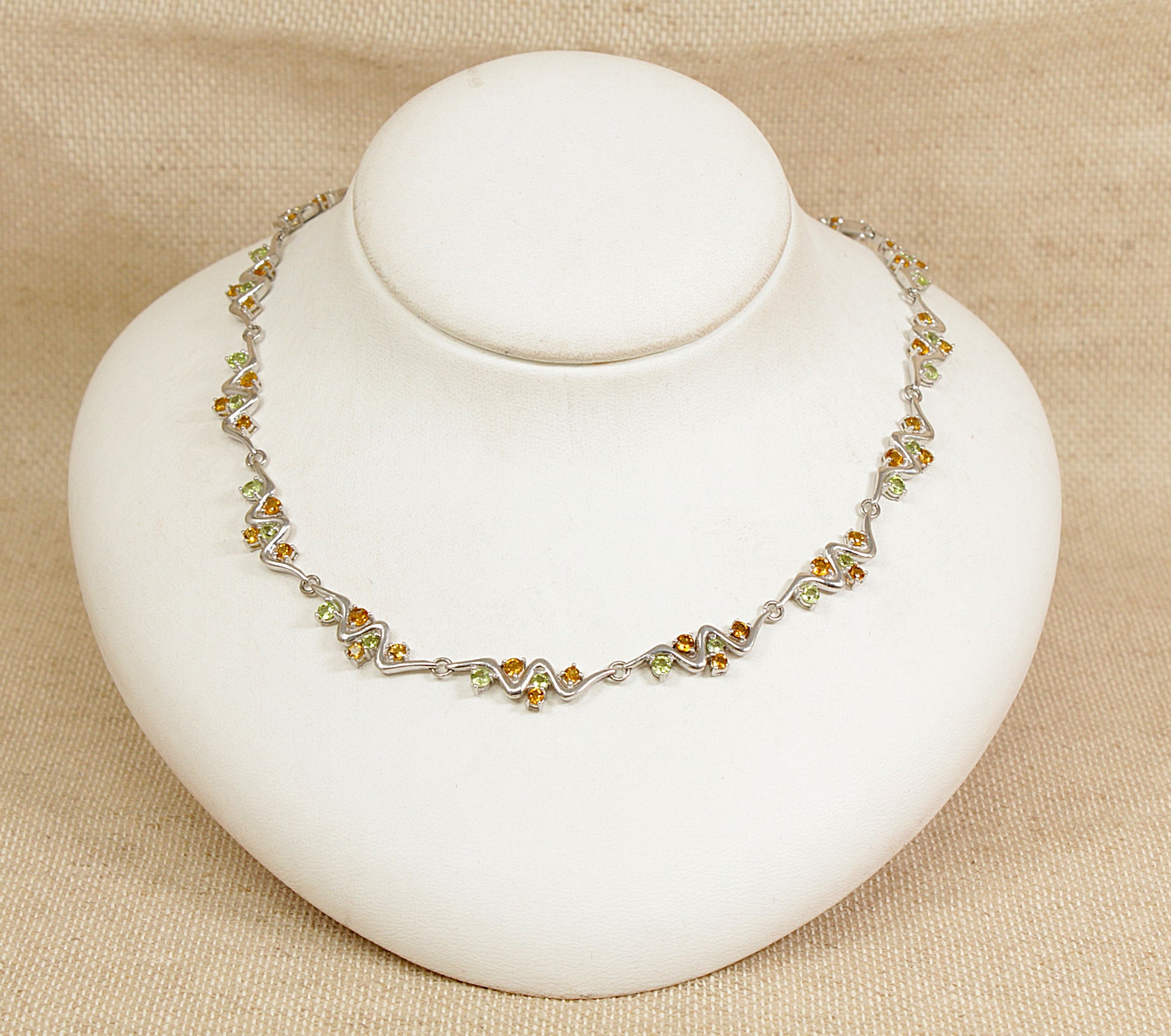 Necklace with citrine and peridot gemstones on a white stand against a beige background