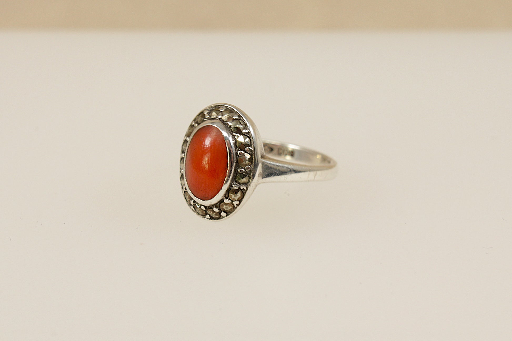 Silver ring with red coral surrounded by a halo of marcasite gemstones on a beige background