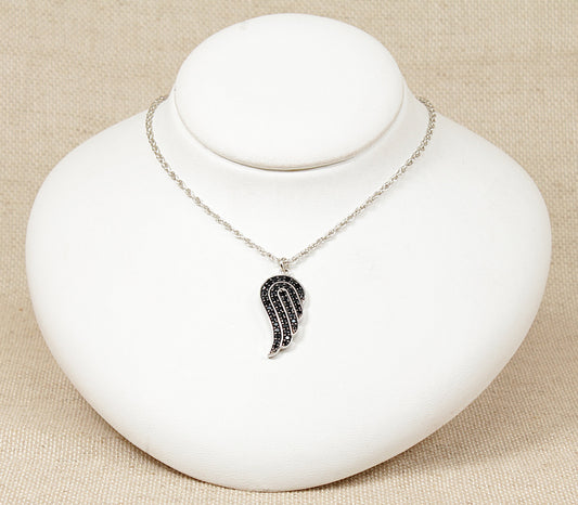 A silver pendant designed in the form of an angel's wing, encrusted with midnight blue round crystals, displayed on a white bust.