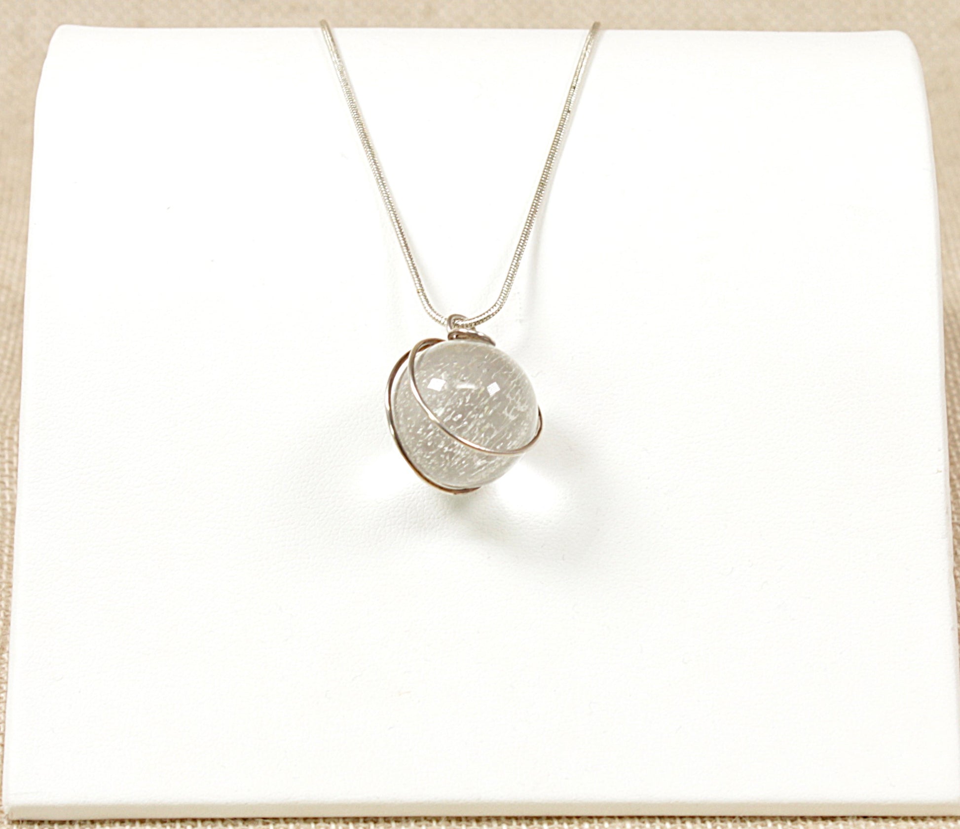 This pretty Silver pendant has a round Quartz Crystal ball set into a decorative silver setting. The pendant sits on a 22 inch silver snake chain. The chain is stamped 925 for sterling silver.