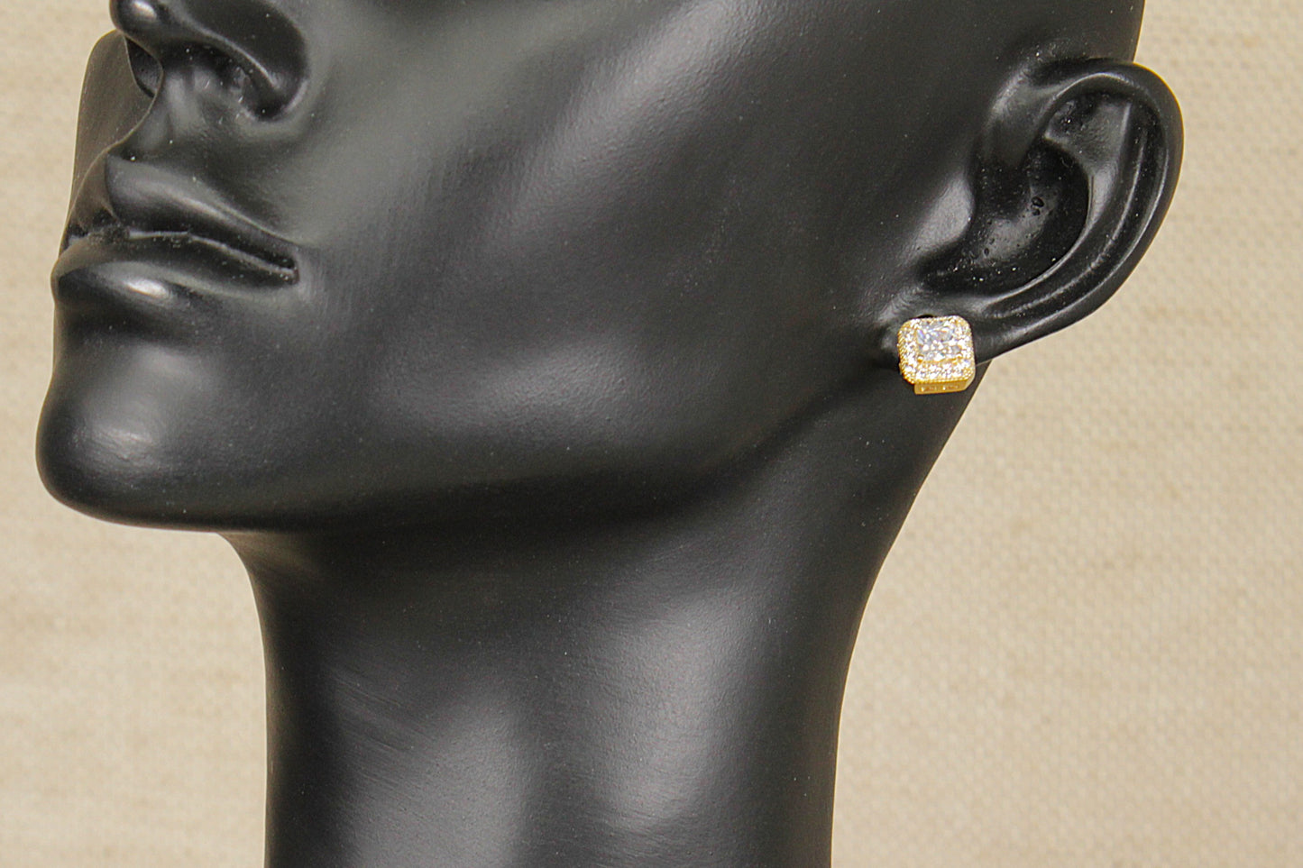 Silver gilt and cz earring on a black mannequin head against a beige background