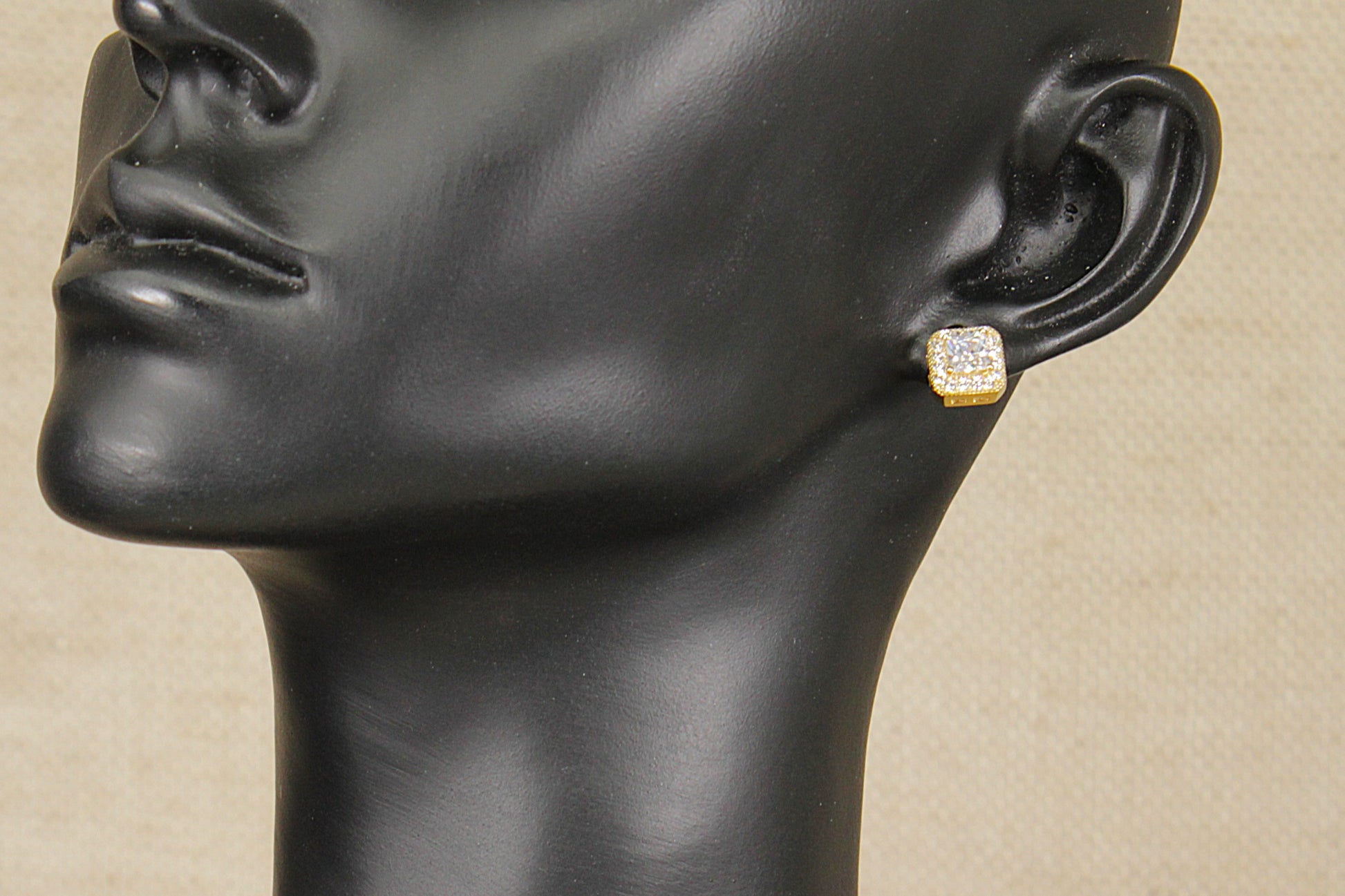 Silver gilt and cz earring on a black mannequin head against a beige background