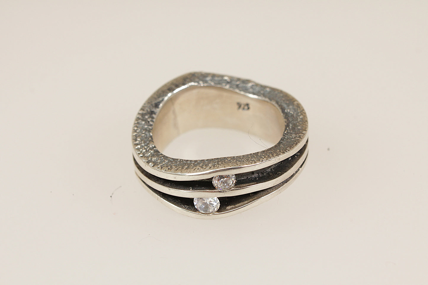 Silver ring with embedded crystal gemstones on a light beige background
