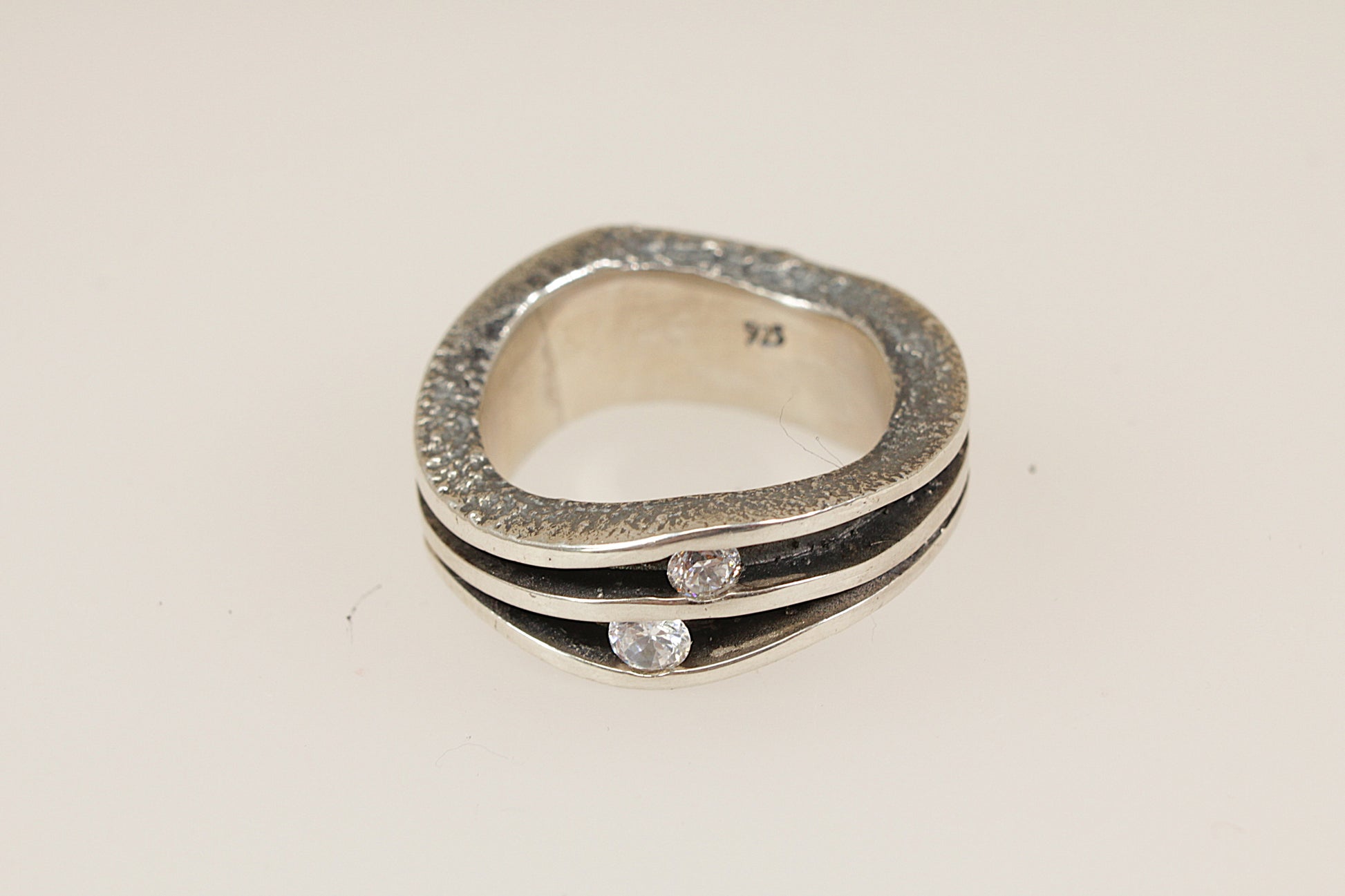 Silver ring with embedded crystal gemstones on a light beige background