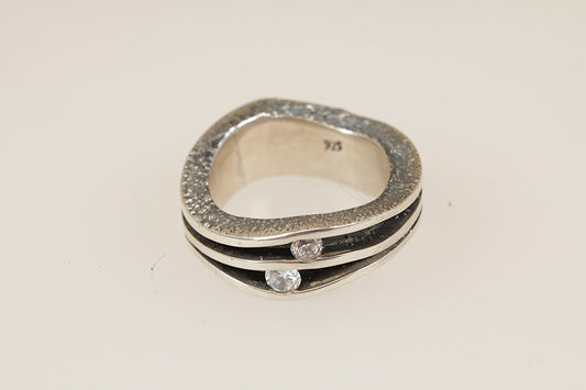 Silver ring with embedded crystal gemstones on a light beige background