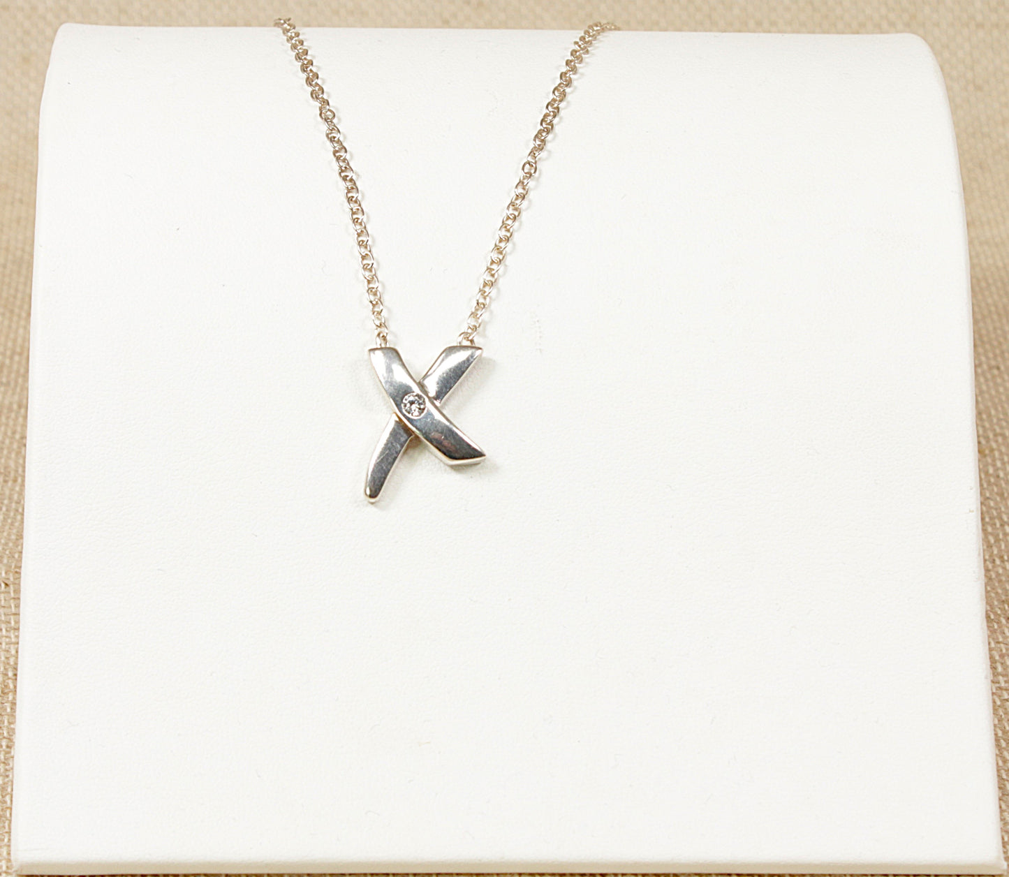 This charming Silver pendant is in the form of an ‘X’ set with a round faceted Cubic Zirconia gemstone set into the middle of the ‘X’. The pendant is attached to an 18 inch Belcher style chain, stamped 925 for sterling silver.