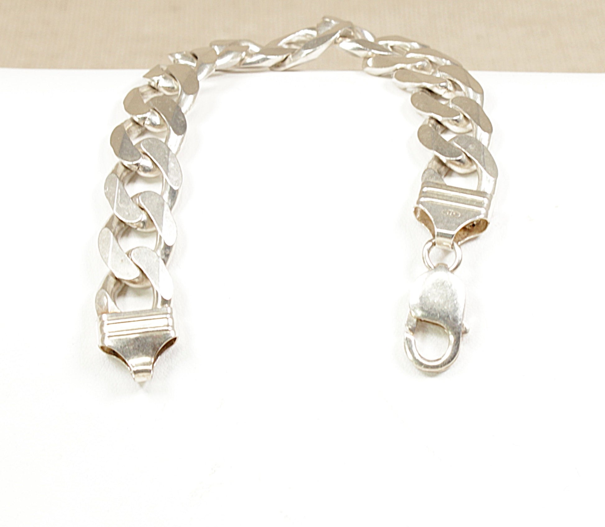 A sterling silver flat curb link bracelet displayed on a black surface.