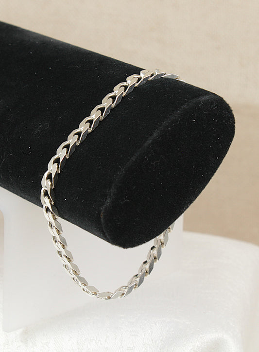 Silver flat curb link chain bracelet on a black velvet stand with a neutral background