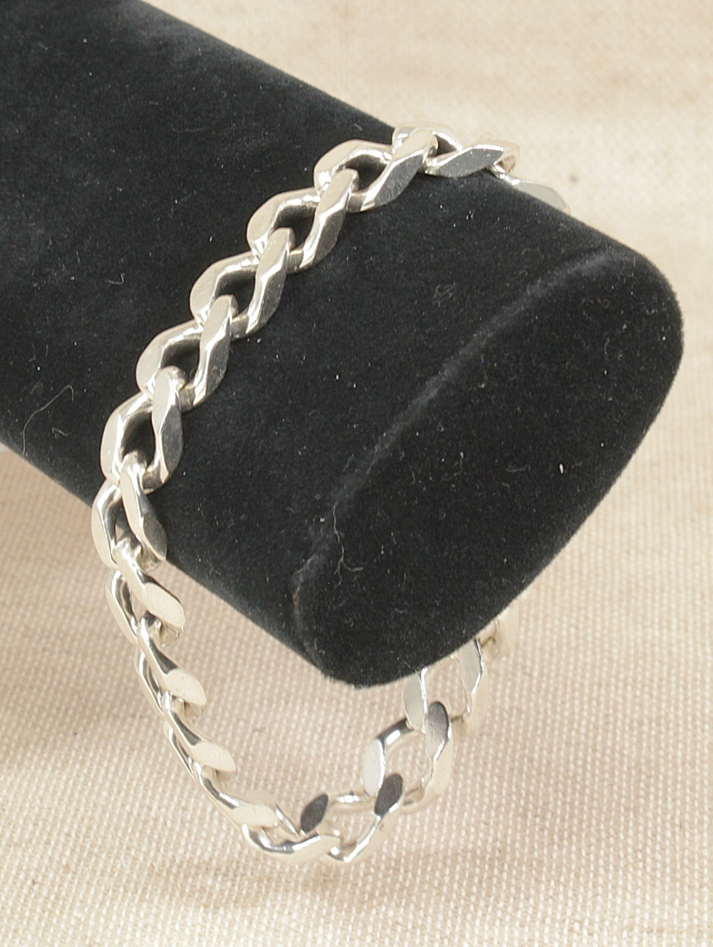 Silver flat curb link chain bracelet on a black velvet stand with a beige background
