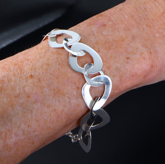 A silver designer link bracelet with large and small curved, rounded triangular links displayed on a person's wrist.