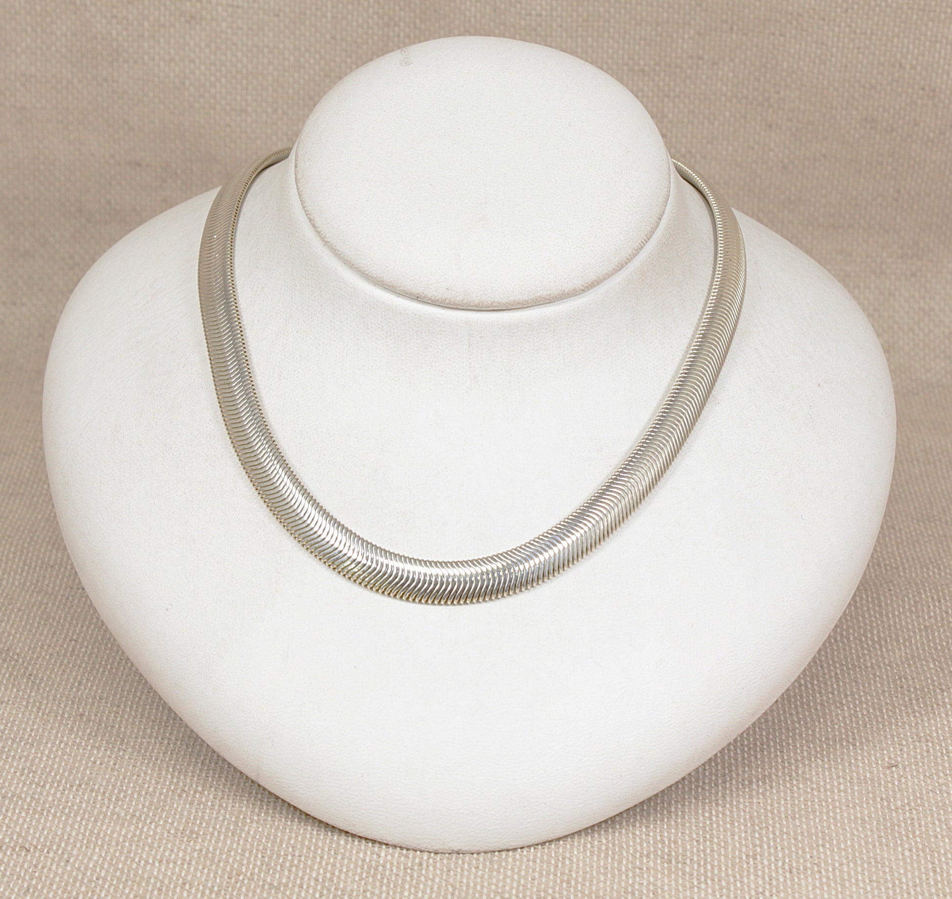 Silver necklace on a white bust against a beige background