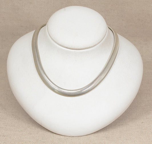 Silver necklace on a white bust against a beige background
