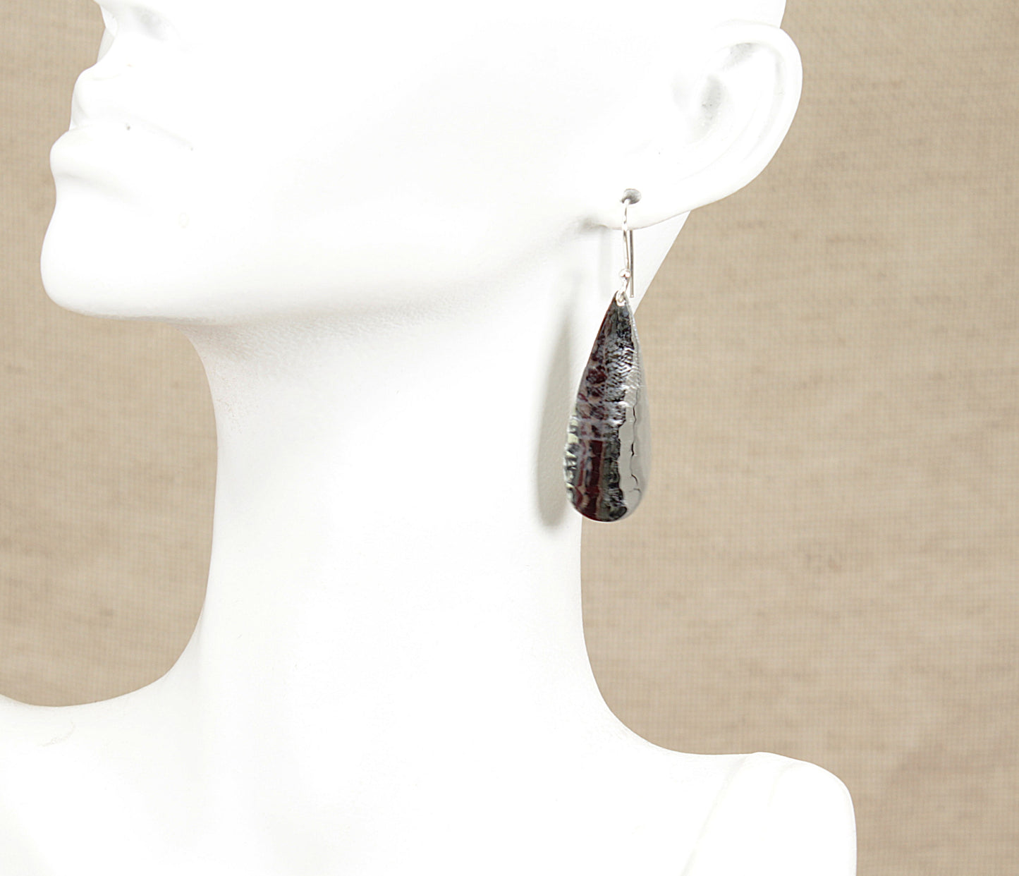 Teardrop-shaped silver earrings on a mannequin with a neutral background