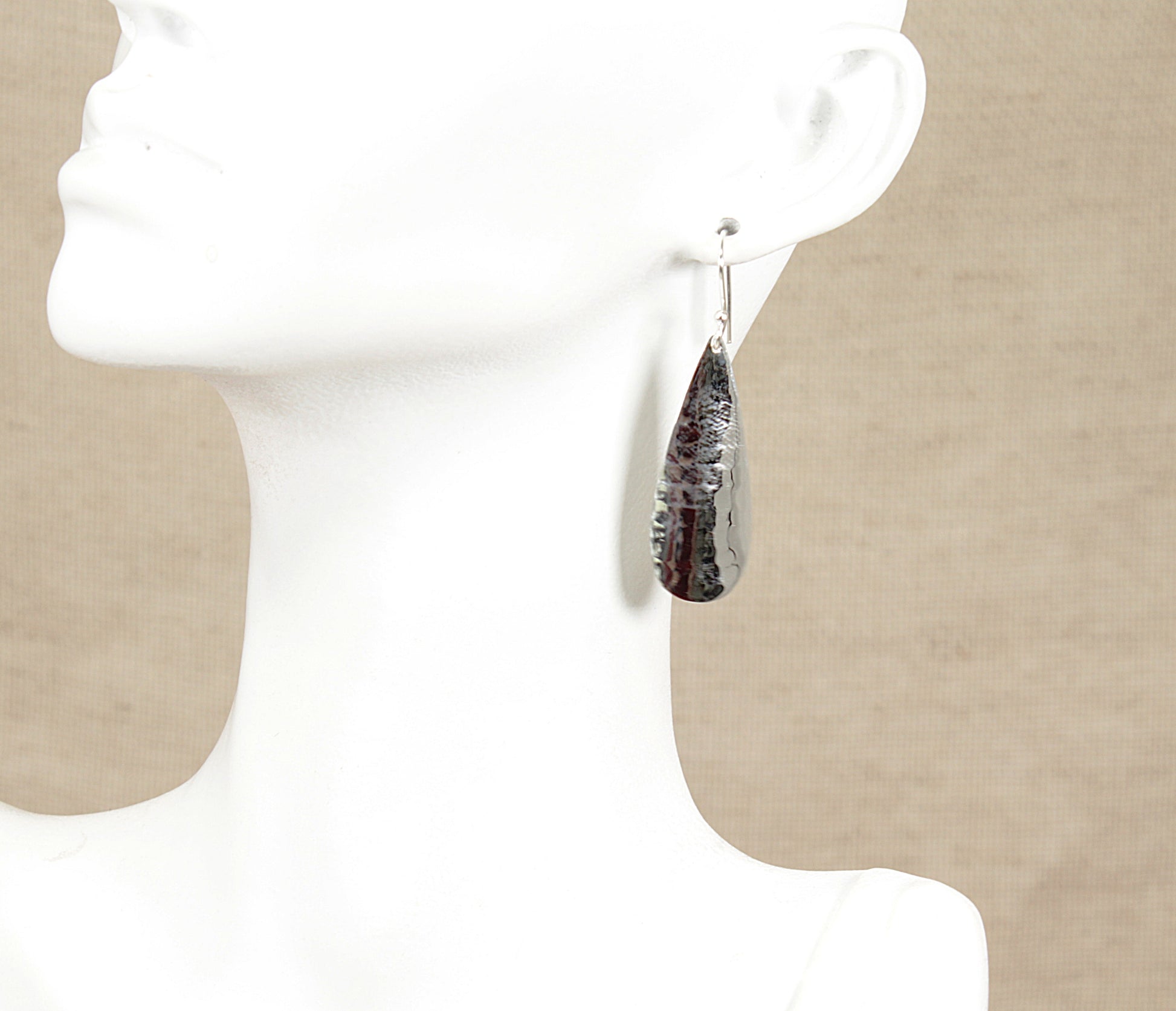 Teardrop-shaped silver earrings on a mannequin with a neutral background