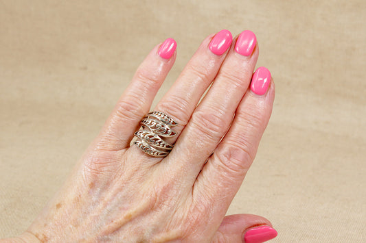 Hand with pink nail polish wearing a silver statement ring on a beige background