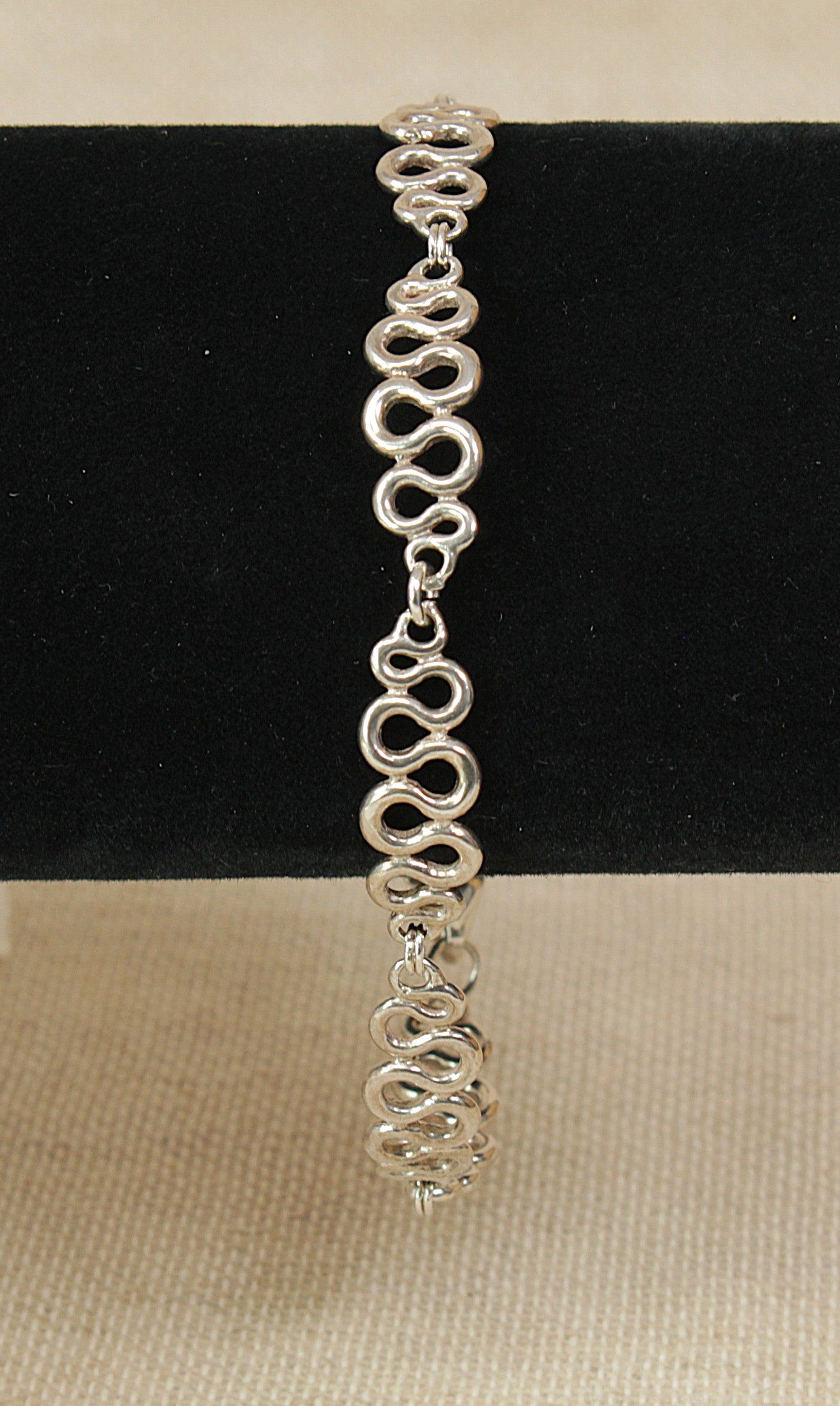 Silver fancy swirly link bracelet with heart charm on a black bracelet stand with a beige background
