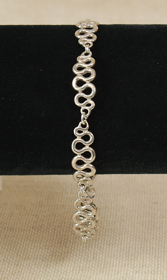 Silver fancy swirly link bracelet with heart charm on a black bracelet stand with a beige background