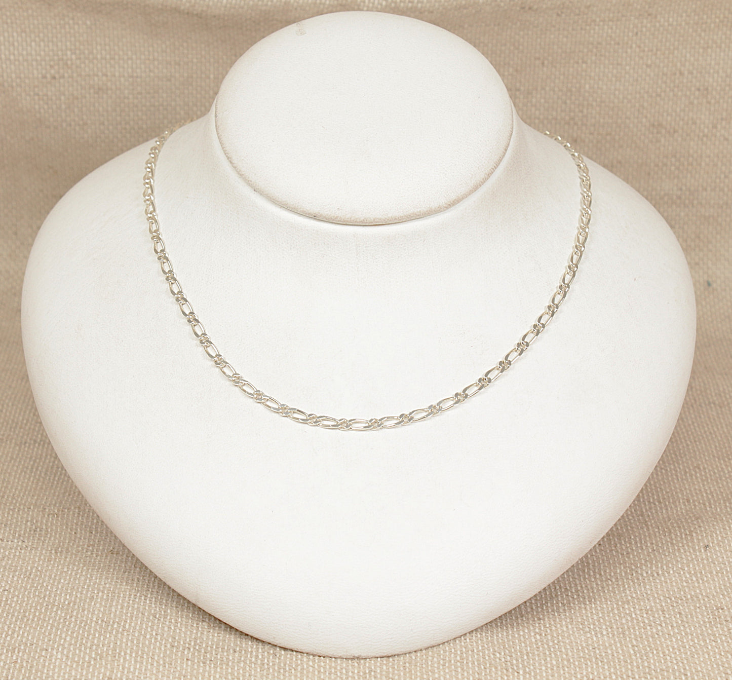 Silver figaro necklace chain on a white bust against a beige background