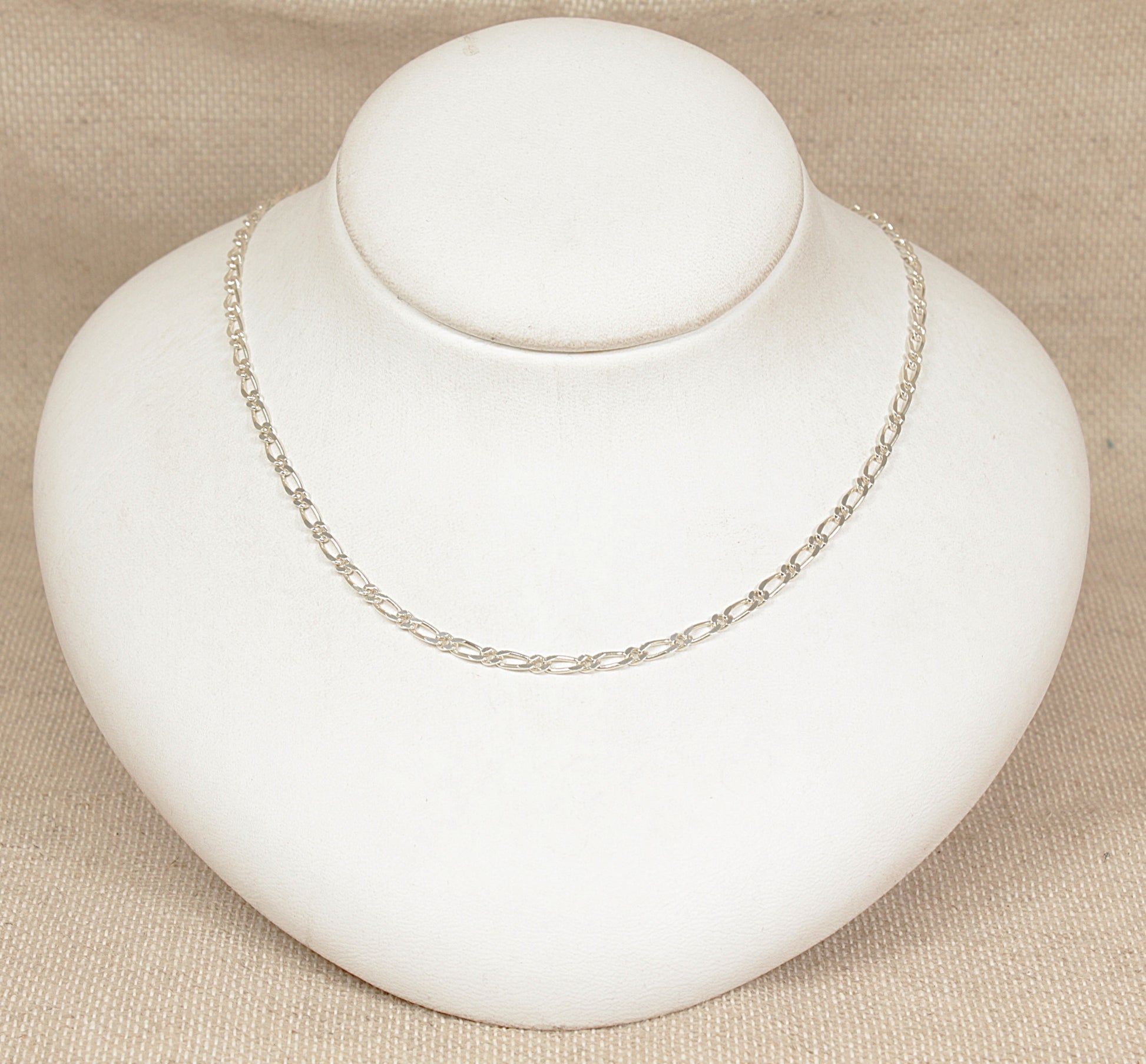 Silver figaro necklace chain on a white bust against a beige background
