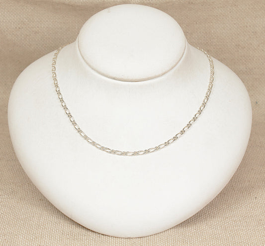 Silver figaro necklace chain on a white bust against a beige background