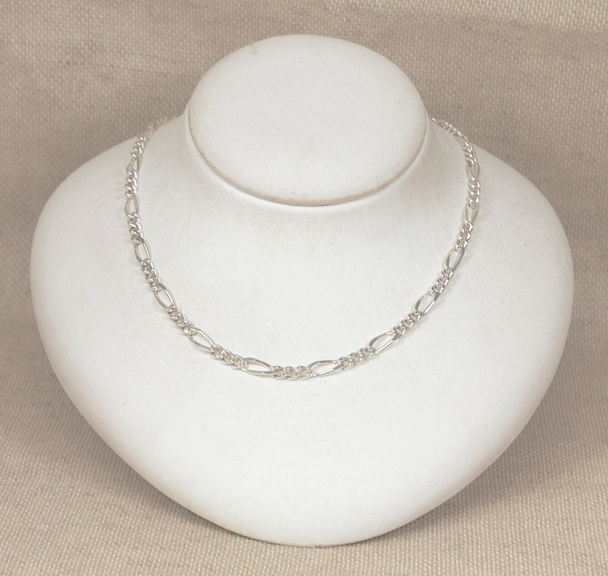 Silver figaro link necklace chain on a white mannequin bust against a beige background