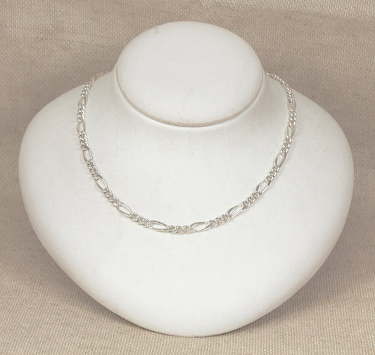 Silver figaro link necklace chain on a white mannequin bust against a beige background