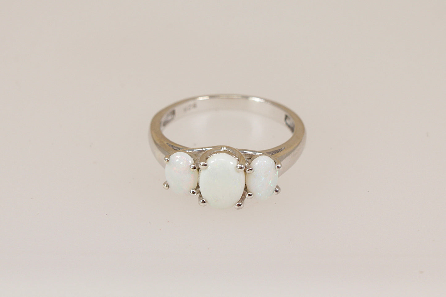 Silver ring with three opal gemstones on a beige background