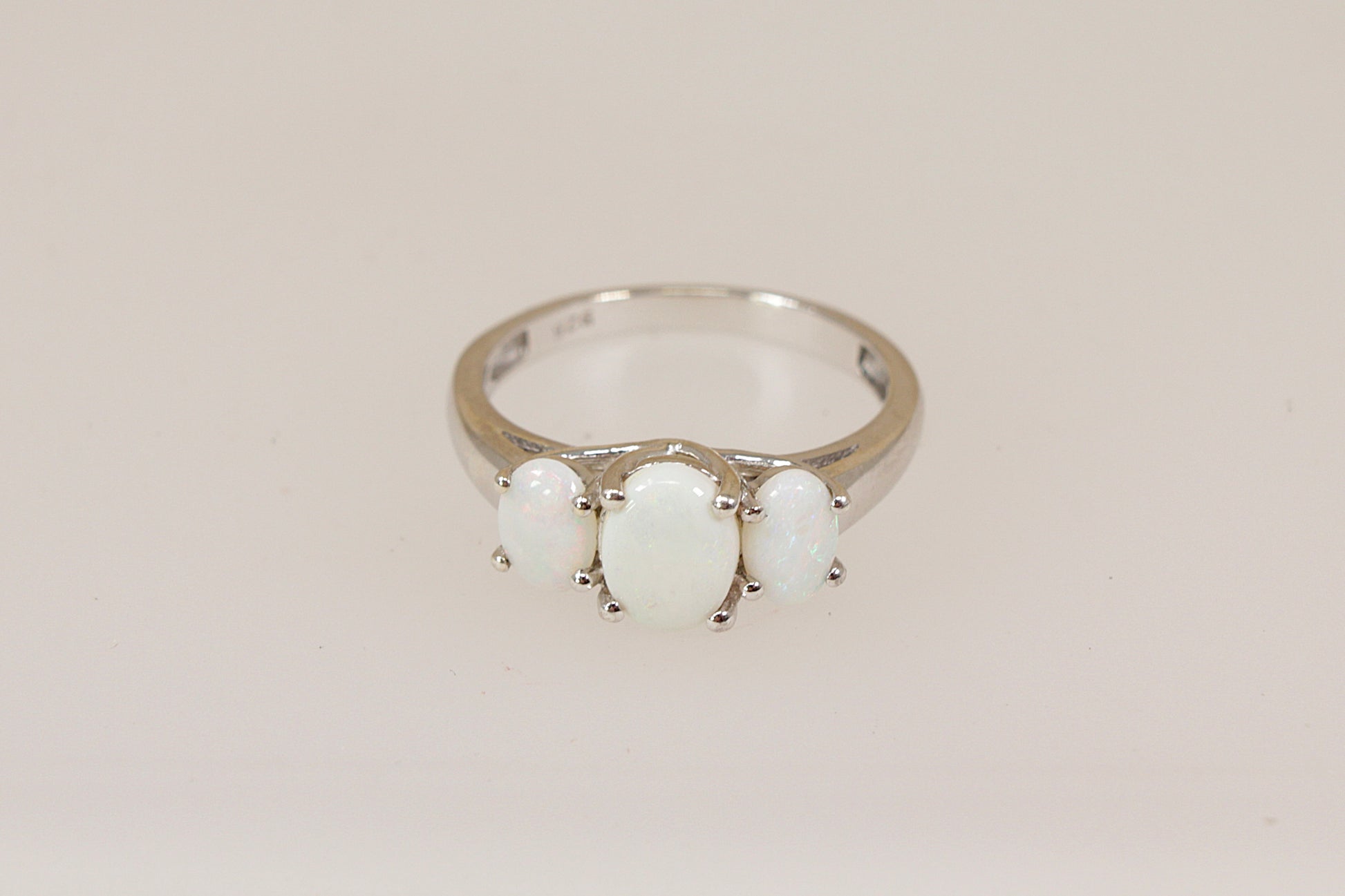 Silver ring with three opal gemstones on a beige background