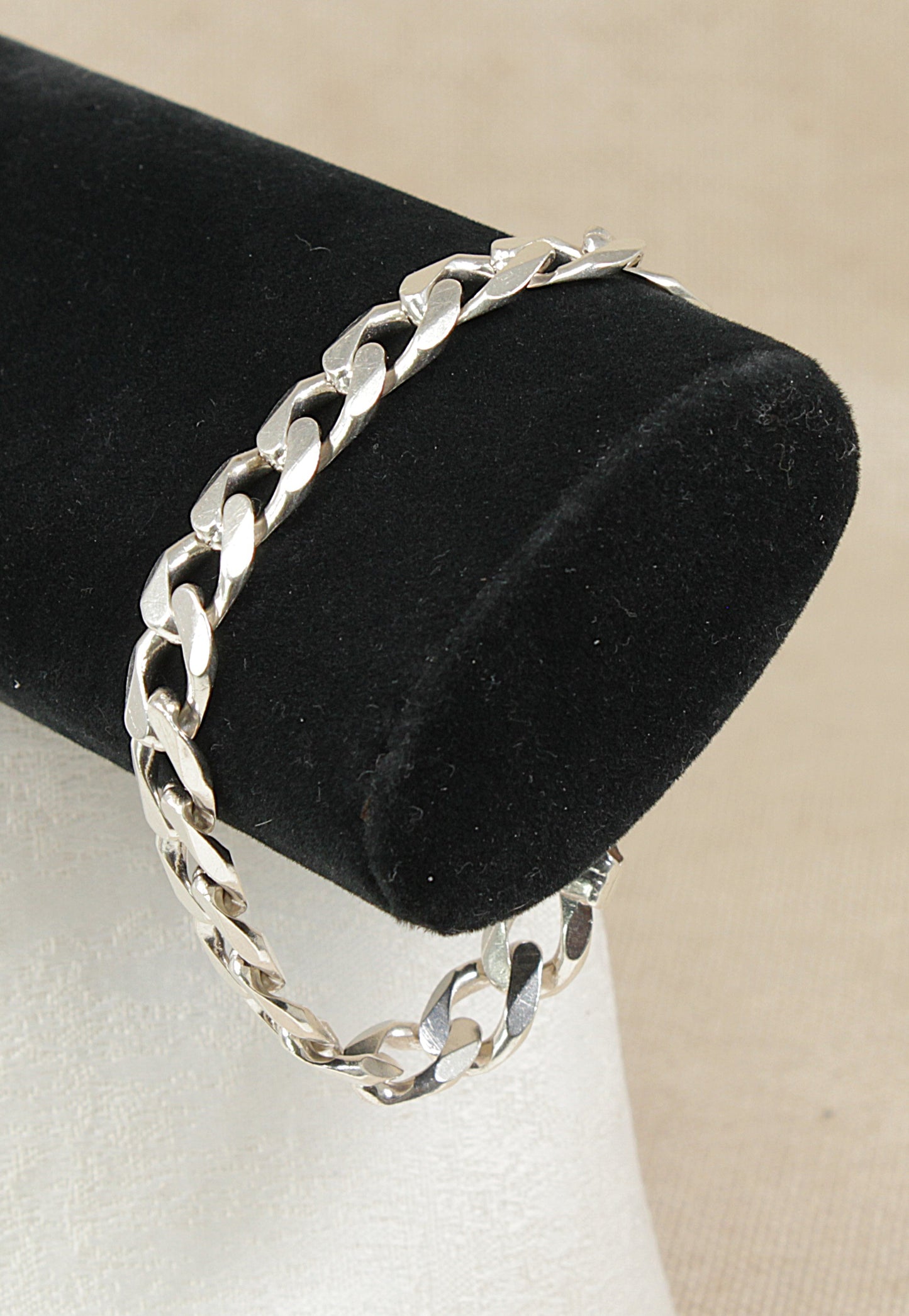Silver flat curb link chain bracelet on a black velvet stand with a beige background