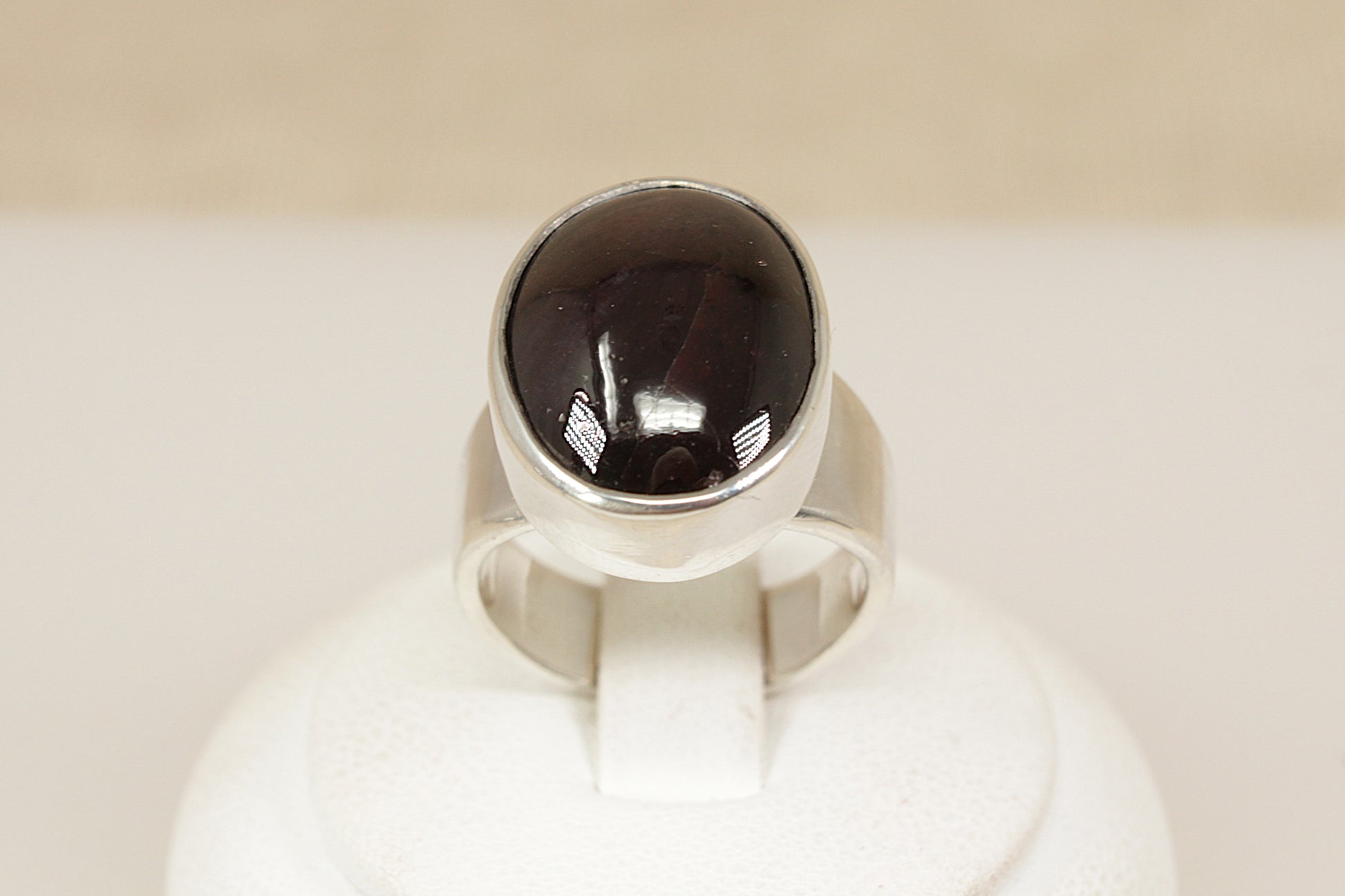 A striking and beautifully crafted sterling silver statement ring, showcasing a large cabochon-cut garnet with a rich, deep red hue. The garnet is set in a deep-sided bezel, giving the piece a bold, sculptural presence while highlighting the smooth, glossy surface of the gemstone. UK finger size O.