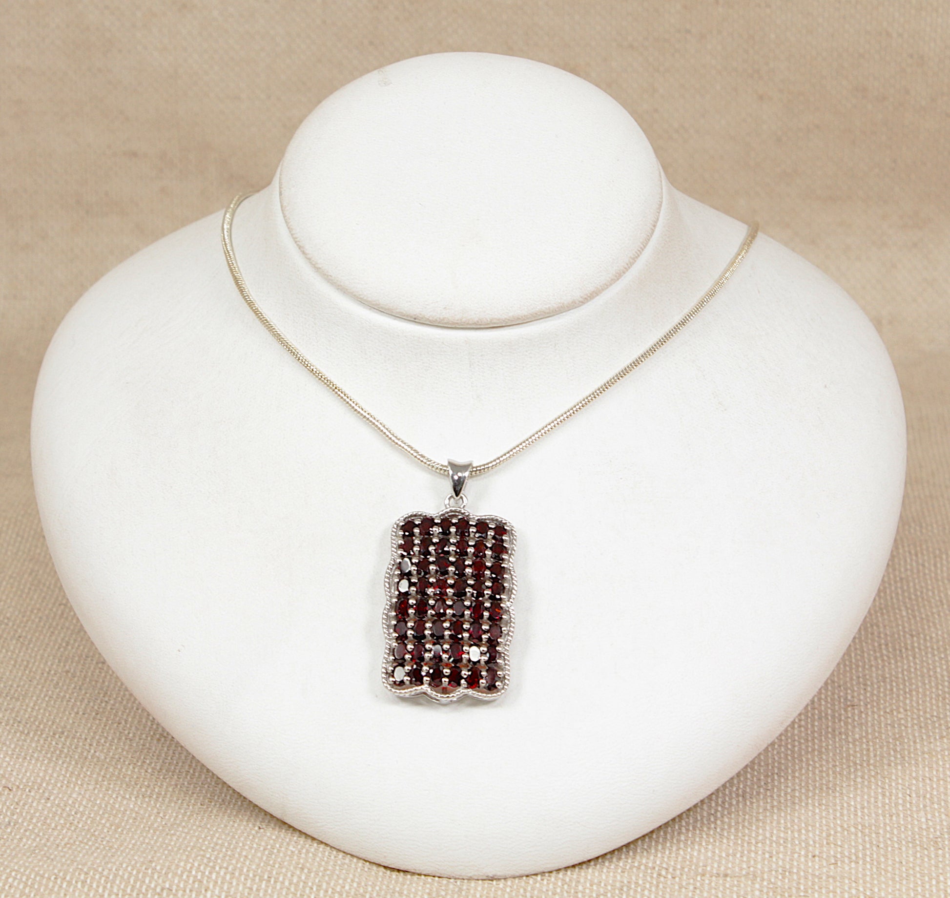 Silver pendant set with rich red garnets with a silver chain on a white bust with a beige background 