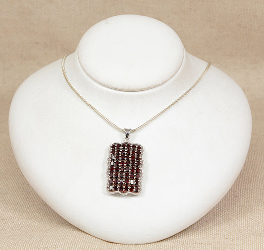 Silver pendant set with rich red garnets with a silver chain on a white bust with a beige background 