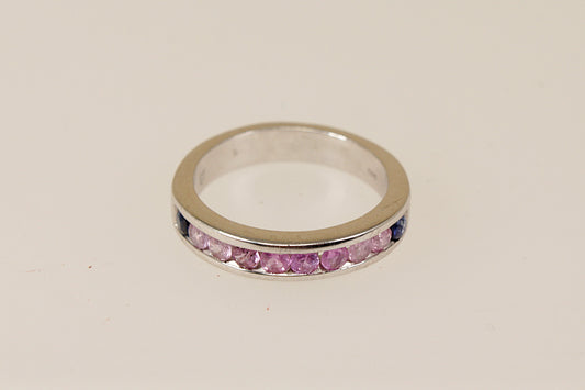 A sterling silver half eternity ring with a series of round-cut pink topaz gemstones channel-set within the band, with two deep blue sapphire stones at each end.