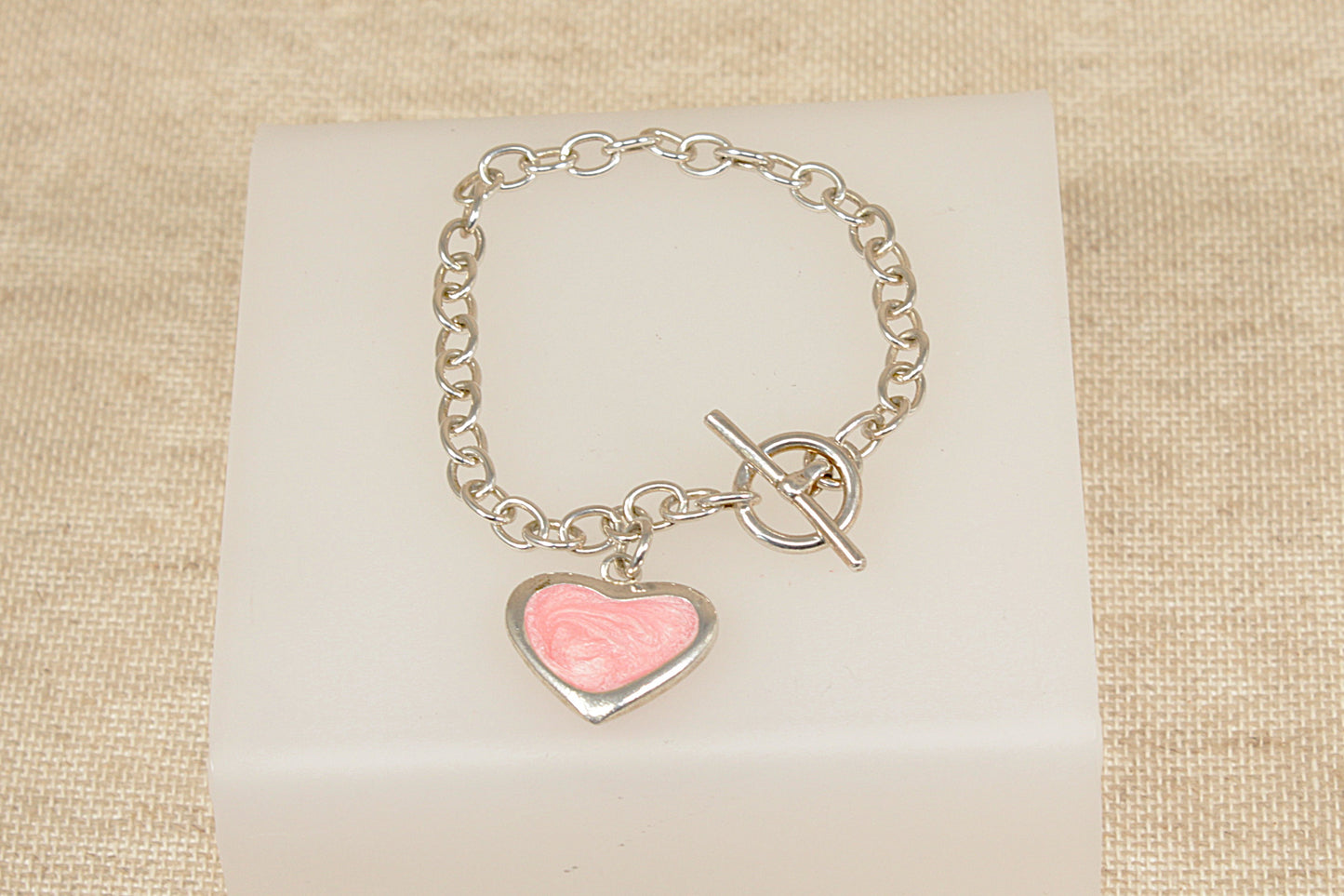 Silver bracelet with a pink heart charm on a beige fabric background