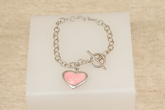 Silver bracelet with a pink heart charm on a beige fabric background