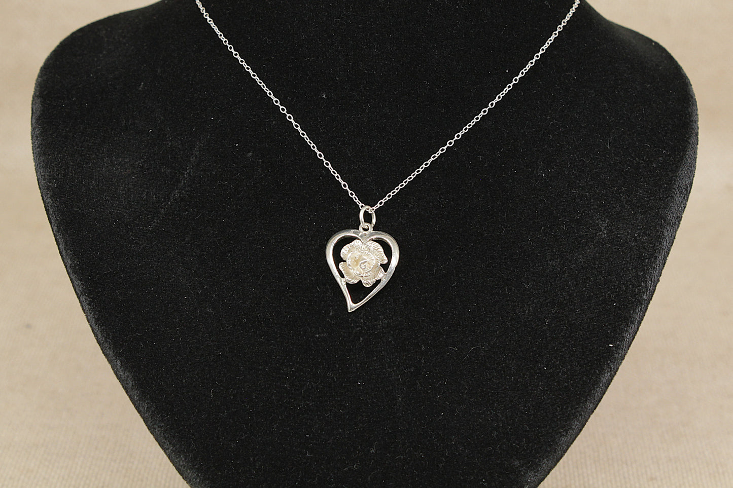 Necklace with a heart-shaped pendant featuring a rose on a black velvet stand.