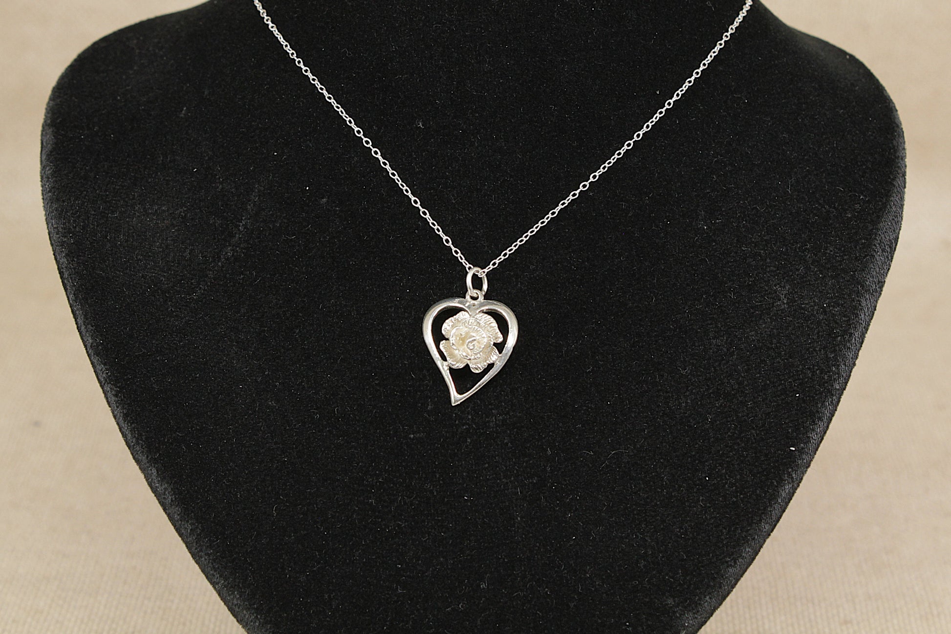 Necklace with a heart-shaped pendant featuring a rose on a black velvet stand.
