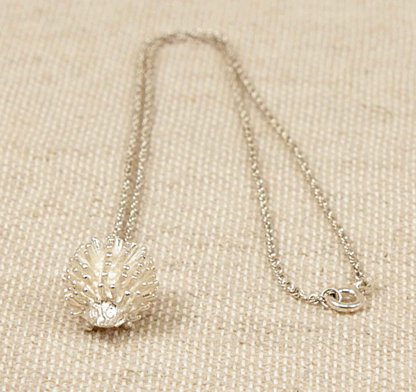 A sterling silver hedgehog pendant with a 'Prince of Wales' silver chain necklace laid out on a textured surface.